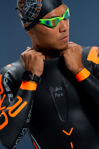 Front close-up of male athlete wearing Rocket Science Sports Viper wetsuit, adjusting collar, showing Ultra Flex chest panel and orange wrist cuffs