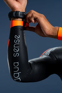 Close-up of athlete adjusting wrist cuff on Rocket Science Sports Aquasense wetsuit, showing aqua sense sleeve branding and snug seal