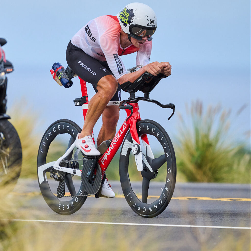 Cyclist in action with a motorcycle following closely on a road.